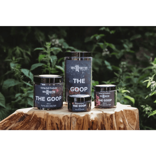 Soil Smiths The Goop — four sizes of dark amber Goop jars on tree stump, leafy backdrop