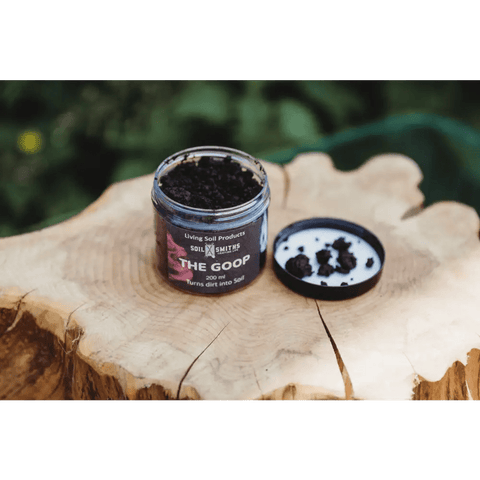 Soil Smiths The Goop — open amber jar of dark microbial paste with Soil Smiths label on wooden tree stump