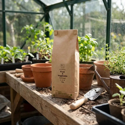 Organic Fruit & Vegetable Fertiliser — kraft bag in sunlit greenhouse on potting bench with terracotta pots and trowel