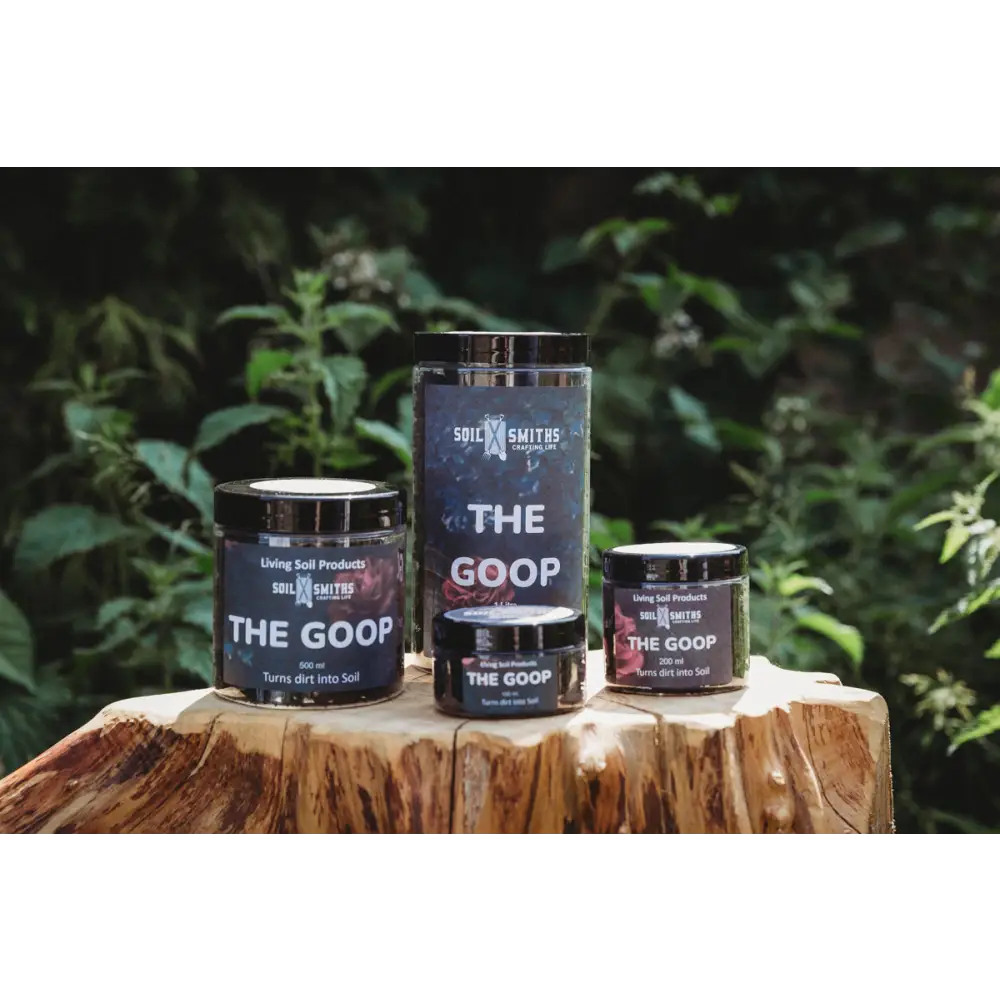 Soil Smiths The Goop — four sizes of dark amber Goop jars on tree stump, leafy backdrop