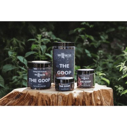 Soil Smiths The Goop — four sizes of dark amber Goop jars on tree stump, leafy backdrop
