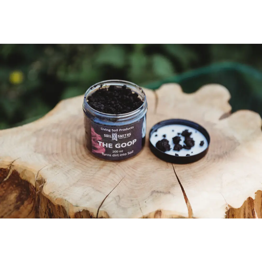 Soil Smiths The Goop — open amber jar of dark microbial paste with Soil Smiths label on wooden tree stump