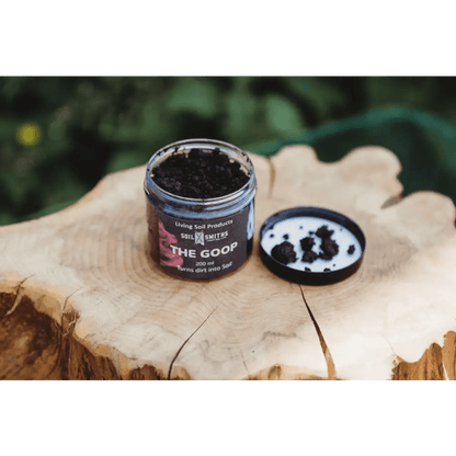 Soil Smiths The Goop — open amber jar of dark microbial paste with Soil Smiths label on wooden tree stump