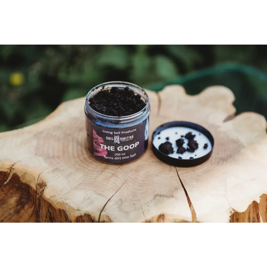 Soil Smiths The Goop — open amber jar of dark microbial paste with Soil Smiths label on wooden tree stump